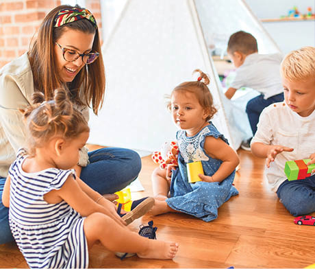 Beautiful teacher and group of toddlers playing around lots of toys at kindergarten